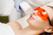 A woman wearing orange protective eyewear receives a facial treatment with a laser device handled by a person wearing gloves.